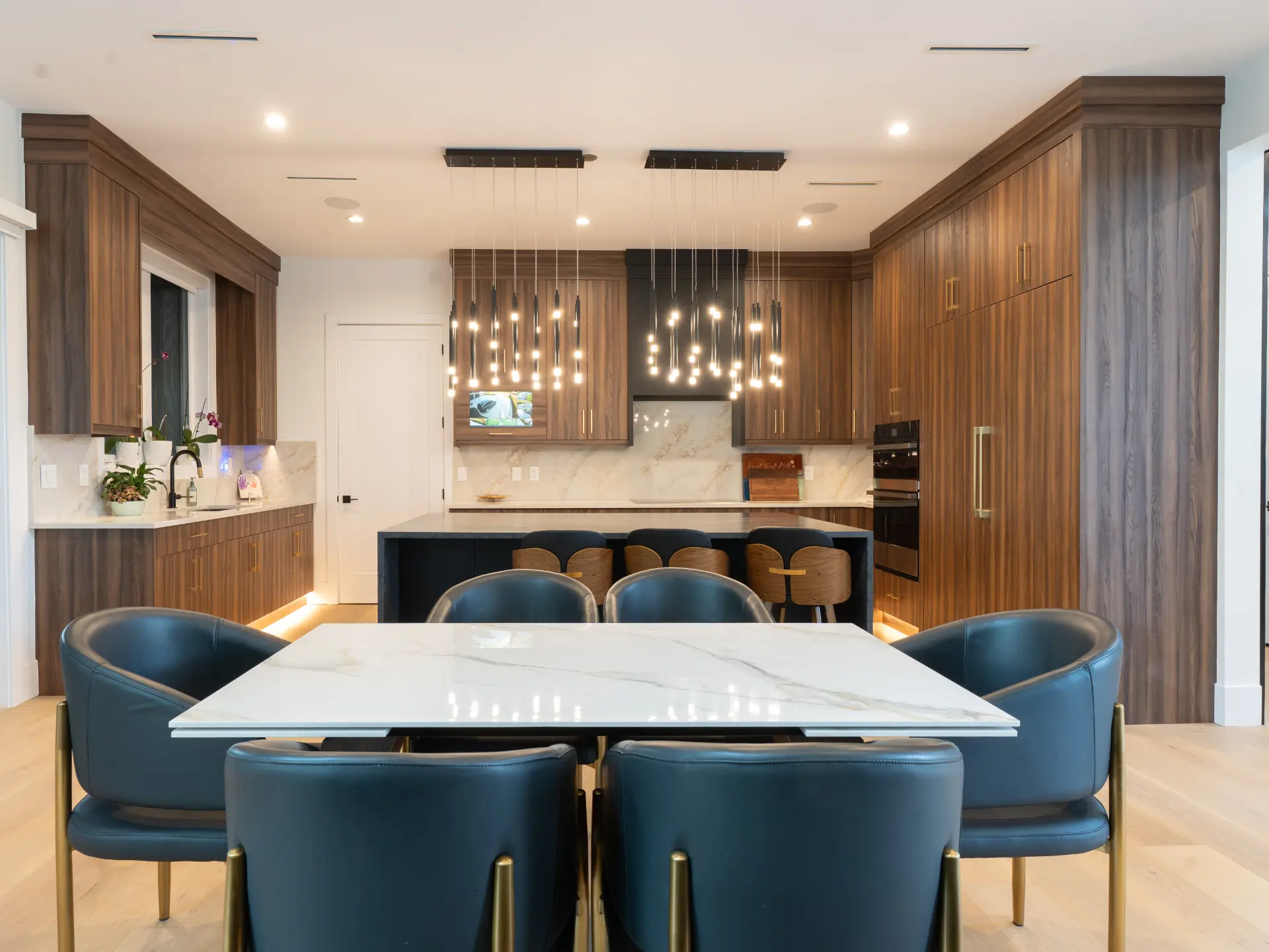 Bright open dining and kitchen space with walnut cabinetry, stone table, and pendant lighting