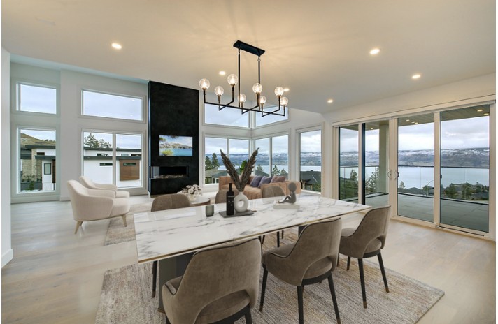 Open-concept living and dining room with a marble dining table, black fireplace column, and sliding doors to a lake view