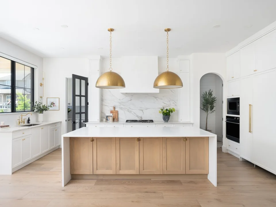 Bright custom kitchen with white cabinetry, an oak island, and brass pendant lights